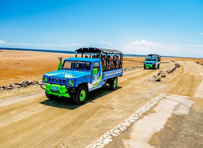 A blue open-sided AGW safari truck on a sandy road in Aruba