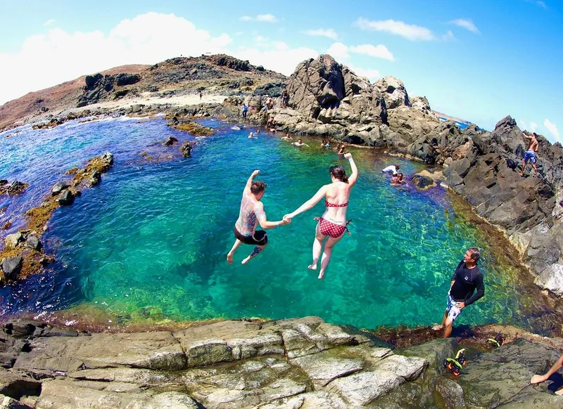 Zwei Personen springen von den Felsen in den Natural Pool auf Aruba